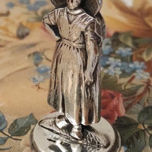 Antico sigillo in ceralacca da scrivania, in argento, raffigurante una donna con un grande cappello, probabilmente olandese. Base con monogramma.