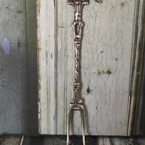 May include: A silver fork with a decorative handle in the shape of a bird. The fork is approximately 15 cm long.