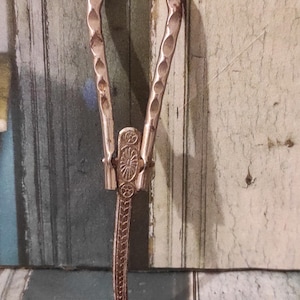 May include: Antique silver-colored metal button hook with a curved handle and a hook at the end. The handle has a decorative design with a series of oval indentations. The hook is designed to assist with buttoning shoes, gloves, or clothing.