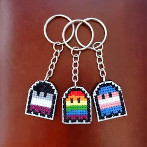 Puede incluir: Cuatro llaveros con diferentes banderas del orgullo en forma de fantasma. Las banderas son la bandera del orgullo asexual, la bandera del orgullo arcoíris, la bandera del orgullo transgénero y la bandera del orgullo bisexual.
