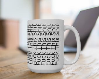 Puede incluir: Taza de cerámica blanca con el texto "Fuck This Shit" repetido verticalmente en negro. La taza tiene un asa grande y está sobre una superficie de madera. Un portátil es visible en el fondo.