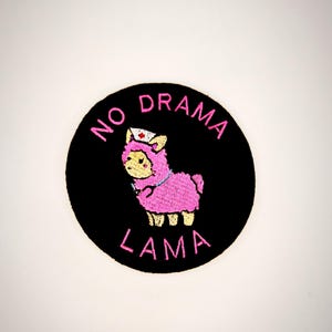 Könnte beinhalten: Ein gestickter Aufnäher in Schwarz und Rosa mit einem Lama, das eine Krankenschwestermütze trägt. Der Text "NO DRAMA LAMA" ist in Rosa um das Lama herum geschrieben.