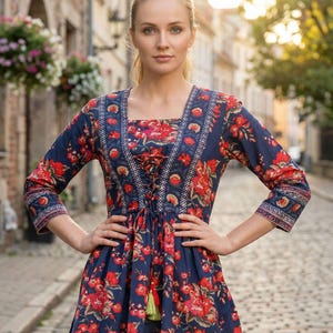 Puede incluir: Vestido túnica azul marino con estampado floral rojo. El vestido presenta un escote cuadrado, mangas tres cuartos y cintura con cordón. El vestido tiene un detalle de borla y está hecho de una tela ligera.
