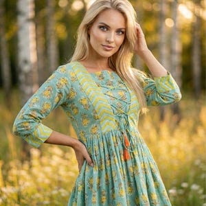 Teal green cotton print kurti for women with yellow floral block print design, handmade Indian ethnic tunic top with lace up neckline and tassel detail, soft breathable summer cotton kurta for casual daily wear, boho style printed kurti paired with black leggings, lightweight spring outfit for women, handcrafted floral cotton kurta for office wear and festive occasions, traditional Indian block print tunic with 3/4 sleeves, comfortable relaxed fit cotton kurti for vacation travel,
