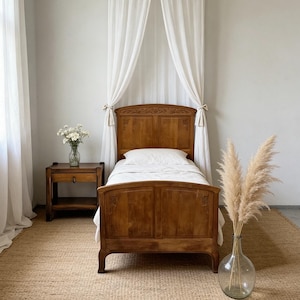 May include: A wooden bed frame with carved floral details on the headboard and footboard, dressed in white bedding. A matching wooden nightstand with a drawer sits to the left, and a clear glass vase with pampas grass stands to the right.