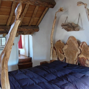 May include: A wooden bed frame with a unique headboard made from natural wood slices. The bed has a dark blue comforter and is in a rustic room with exposed wooden beams.