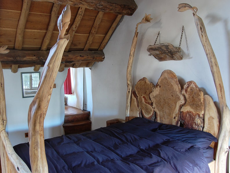 May include: A wooden bed frame with a unique headboard made from natural wood slices. The bed has a dark blue comforter and is in a rustic room with exposed wooden beams.