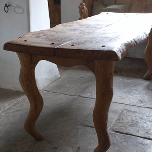 May include: A rustic wooden table with a live edge top and four unique, curved legs. The table is made of natural wood and has a warm, brown colour.