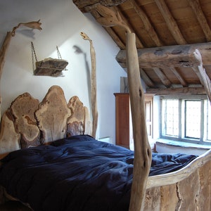 May include: A rustic wooden bed frame with a headboard made of large, natural wood slabs. The bed is covered with a dark blue duvet and has a wooden shelf above the headboard.