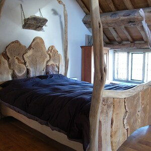 May include: A rustic wooden bed frame with a headboard made of thick, natural wood slabs. The bed is covered with a dark blue duvet and has a simple, natural design.