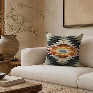 May include: A square throw pillow featuring a symmetrical geometric pattern in shades of charcoal gray, burnt orange, cream, and muted teal. The design consists of concentric diamond shapes radiating from a central point across the fabric surface.