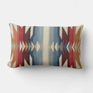 May include: Rectangular decorative pillow with a Southwestern-inspired design. The pillow features a central vertical stripe of blue and cream, flanked by symmetrical patterns in shades of red, orange, and cream. The design includes geometric shapes.