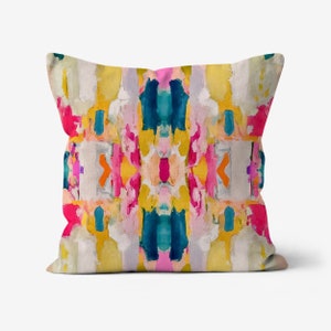 May include: A colorful throw pillow with an abstract design featuring shades of pink, yellow, blue, and orange. The pillow has a white background and a symmetrical pattern.