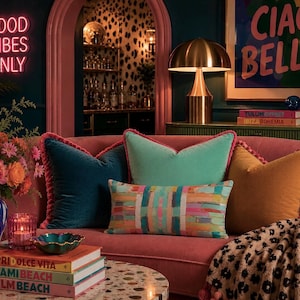 May include: A pink curved sofa features a collection of velvet throw pillows in teal, mint green, and mustard yellow, alongside a rectangular pillow with a colorful abstract pattern and a leopard print throw blanket with pink tassels.
