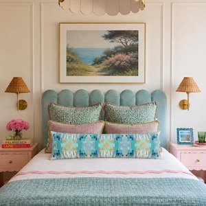 May include: A bedroom featuring a scalloped light blue headboard, a white bedspread with a light blue quilted runner, and a long rectangular pillow with a geometric pattern. The bed is flanked by two pink nightstands with wicker wall sconces.