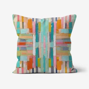 May include: A colorful throw pillow with a geometric pattern of stripes and rectangles in shades of blue, green, orange, pink, and yellow.