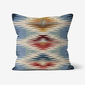 May include: Square throw pillow with a geometric pattern in shades of blue, cream, red, and gold. The design features a repeating, stylized motif reminiscent of Native American textiles. The pillow has a soft, textured appearance.