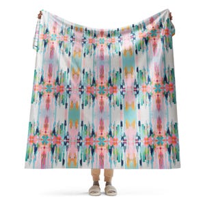 May include: A colorful throw blanket with a geometric pattern in shades of pink, blue, green, and yellow. The blanket has a white background and is made of a soft, comfortable fabric.