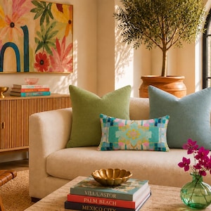 May include: A cream-colored sofa featuring three decorative throw pillows: one solid olive green square pillow, one solid light blue square pillow, and one rectangular pillow with a multicolored geometric pattern in shades of teal, pink, and yellow.