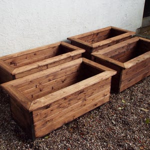 May include: Four wooden planter boxes in various sizes, all made of natural brown wood with a rustic finish. The boxes are stacked on top of each other, with the largest box at the bottom and the smallest box at the top.