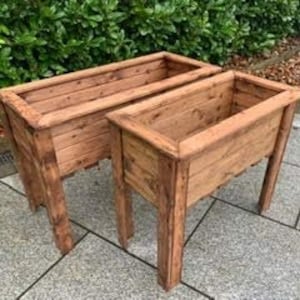 May include: Two wooden planter boxes with a dark brown stain. The boxes are raised on four legs and have a rectangular shape.
