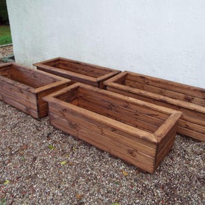May include: Four wooden planter boxes in a dark brown stain. The boxes are lined up in a row, with the largest box at the back and the smallest box at the front.