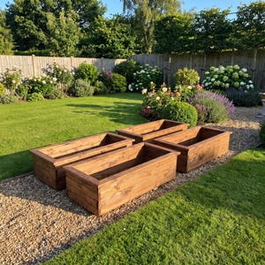 May include: Three rectangular garden planters constructed from dark brown stained wood. Each planter features a flat top rim and vertical side panels, arranged in a cluster on a gravel path. The planters have a hollow interior and a sturdy frame.