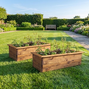 May include: Two rectangular wooden planters with a dark brown finish, each featuring horizontal plank construction and a flat top rim. The planters are filled with green leafy plants and are positioned on a green lawn in an outdoor setting.