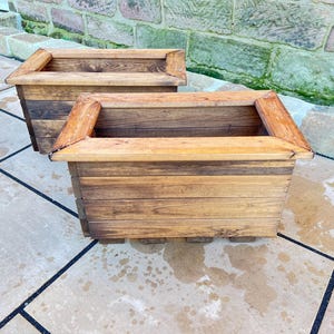 May include: Two wooden planter boxes, one stacked on top of the other. The boxes are made of natural brown wood with a weathered finish.