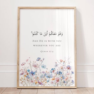 Puede incluir: Una impresión enmarcada con fondo blanco y diseño floral. La impresión presenta una cita árabe en texto negro, "وَهُوَ مَعَكُمْ أَيْنَ مَا كُنتُمْ", que se traduce como "Y Él está contigo dondequiera que estés." La cita va seguida de la traducción al inglés y la referencia "Corán 57:4".