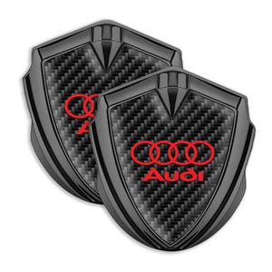 May include: Two black carbon fiber car emblems with a red Audi logo and four rings.