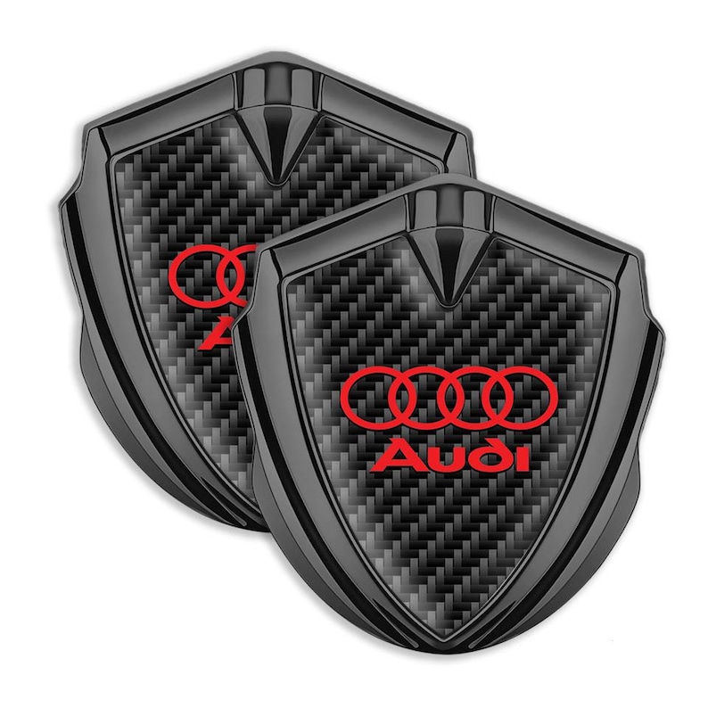 May include: Two black carbon fiber car emblems with a red Audi logo and four rings.