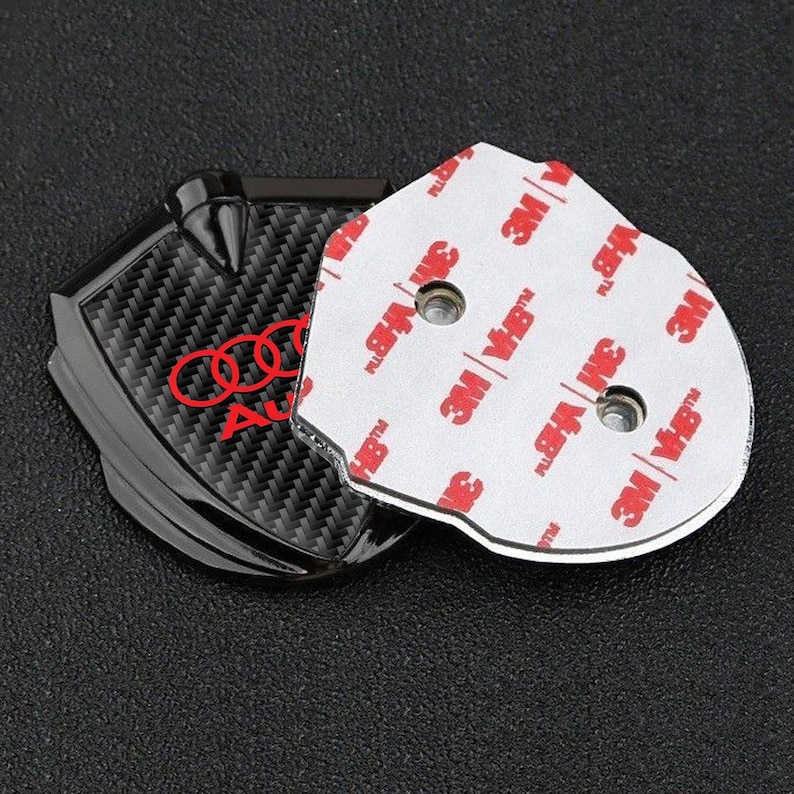 May include: Black carbon fiber car emblem with a red Audi logo and a silver backing with 3M VHB tape.