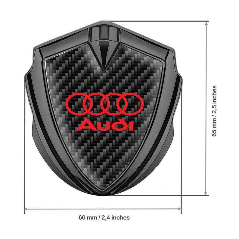 May include: Black car emblem with a carbon fiber pattern and the Audi logo in red. The emblem is 2.4 inches wide and 2.5 inches tall.