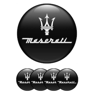 Puede incluir: Cuatro emblemas de coche negros y blancos con el logotipo de Maserati y un tridente. El logotipo es blanco con el texto "Maserati" en blanco.