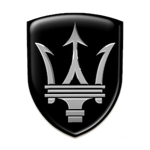 Op de afbeelding: Een zwart en zilveren drietandlogo op een zwarte schildvormige achtergrond. De drietand is een symbool van de Italiaanse luxe autofabrikant Maserati.