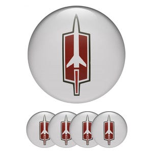 Può includere: Un set di cinque bottoni rotondi bianchi con un emblema rosso e nero. L'emblema è una forma di freccia stilizzata all'interno di un telaio rettangolare. I bottoni sono probabilmente per abbigliamento o accessori.