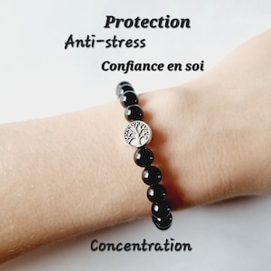 Könnte beinhalten: Schwarzes Perlenarmband mit einem silbernen Lebensbaum-Anhänger. Das Armband befindet sich am Handgelenk einer Person. Der Text "Protection", "Anti-stress", "Confiance en soi" und "Concentration" ist auf dem Bild zu sehen.