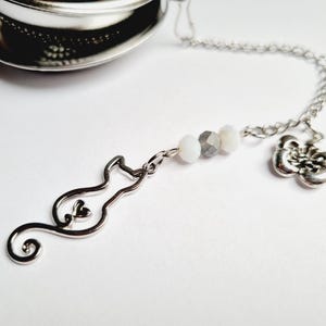 Peut inclure: Infuseur à thé argenté avec un charm en forme de chat, un charm en forme de fleur et des perles décoratives. Le charm chat a un détail en forme de cœur. Conçu pour le thé en vrac.