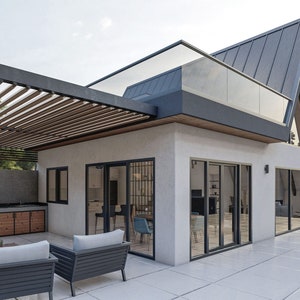 May include: A modern home with a large patio featuring a pergola, outdoor kitchen, and seating area. The home has a unique A-frame design with a large window and a glass railing on the upper level.