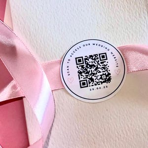 Peut inclure: Un autocollant rond blanc avec un code QR noir, le texte "SCAN TO ACCESS OUR WEDDING WEBSITE" et la date "25.04.25".