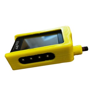 Op de afbeelding: Een gele 3D-geprinte behuizing voor een klein elektronisch apparaat. De behuizing heeft een schermvenster, vier poorten en een kleine zwarte connector aan de zijkant. De tekst "e-SMART" is aan de zijkant van de behuizing gedrukt.