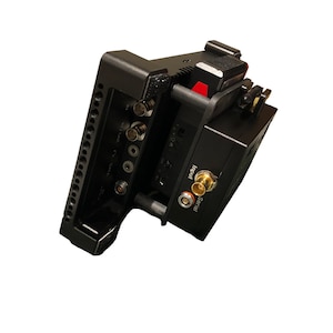 May include: Black camera monitor with multiple ports and connections on the back. The monitor has a metal cage with a cold shoe mount on top.