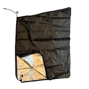 Può includere: Una coperta termica nera e argentata con chiusura a coulisse. La coperta è piegata e parzialmente aperta, rivelando il lato riflettente argentato.