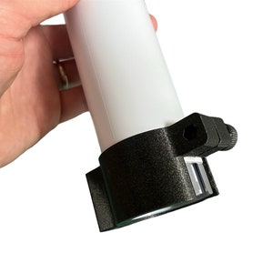 Puede incluir: Una abrazadera de plástico negro con un tubo blanco insertado en ella. La abrazadera tiene un pequeño tornillo en el lateral.