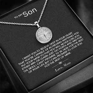 May include: A silver compass necklace with a black box that reads "To My Son" and a message about believing in yourself and achieving your dreams. The box also includes the text "Love, Mom".