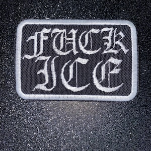 May include: A rectangular black patch with white embroidered text that reads "FUCK ICE" in a gothic font. The patch has a white border and is set against a dark, glittery background.