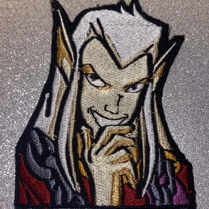 May include: Embroidered patch featuring a stylized character with pale skin, white hair, and pointed ears. The character has a smirk and is wearing a dark outfit with red and purple accents. The patch is outlined in black.