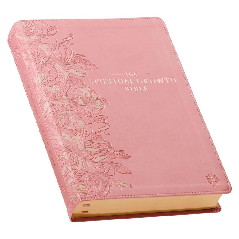 May include: A pink Bible with the title "The Spiritual Growth Bible" in white lettering. The cover features an embossed floral design along the left side. The edges of the pages are gold.