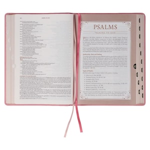 May include: Open Bible with pink cover and matching ribbon bookmark. The pages are filled with text, and a section on Psalms is visible. The book is open, displaying the text and design of the pages.